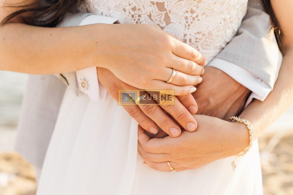 a couple holding a hands together on the girl's belly and wearing rings, anniversary image on zubne.com