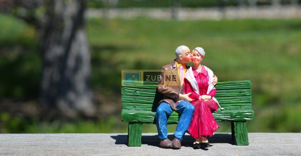 old couple sitting on a wooden bench in park and old guy is kissing the old lady, anniversary images on zubne.com