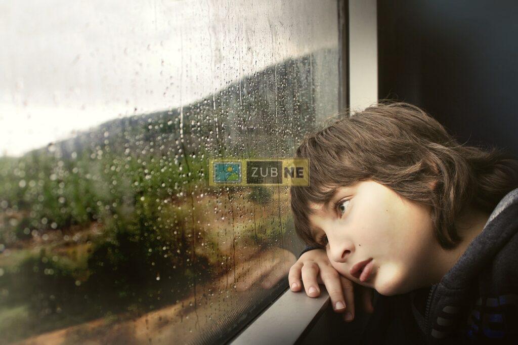 a sad young boy looking outside of the window and its raining outside the window, sad images on zubne.com