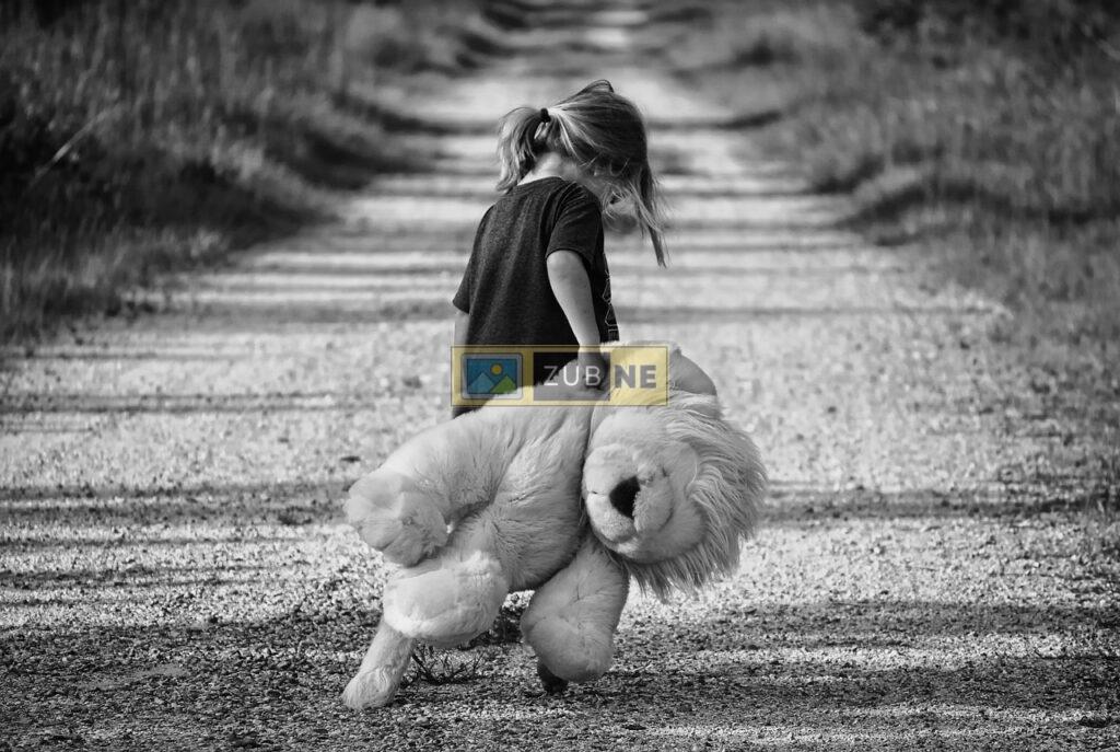 a small young girl in a sad mood walking alone on the road carrying a big teddy bear in her hand, sad images on zubne.com