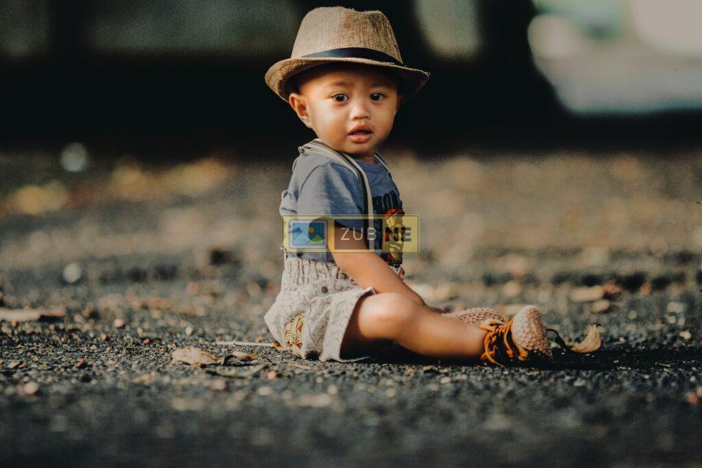 a baby is sitting on the ground. he is wearing a hat,  a t-shirt and a short. Free Baby Images
