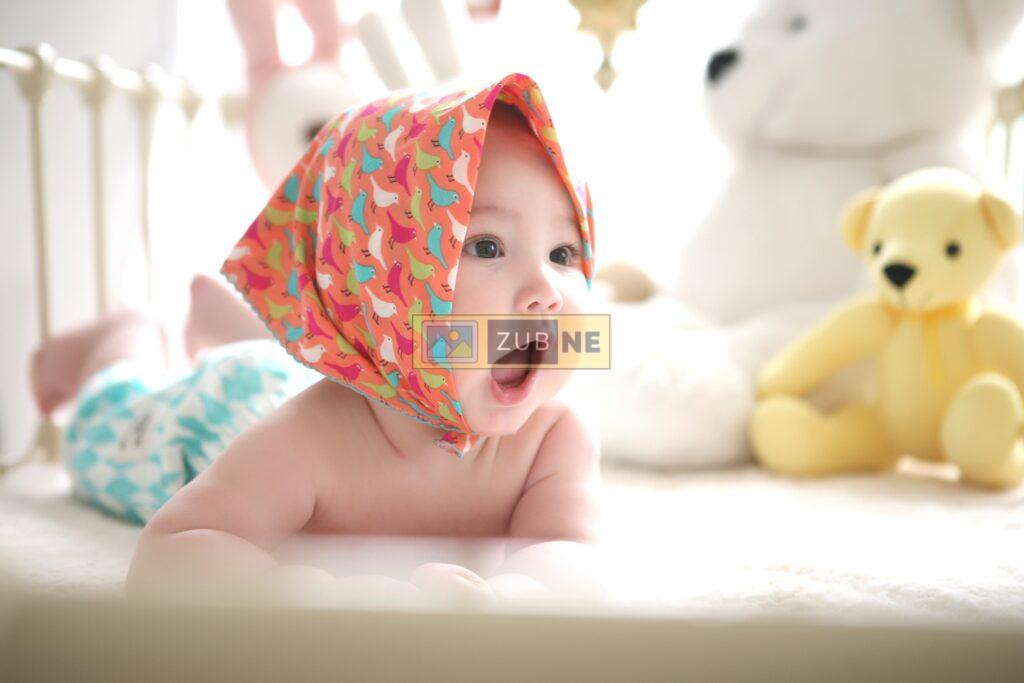 newborn baby lying on bed and wearing a colourful scarf on his head and looking at something.