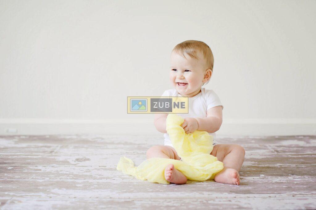 A baby is sitting on floor and wearing a dress and he is smiling 